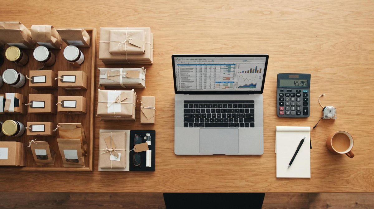 Un escritorio con paquetes, un portátil, calculadora, libreta y taza de café