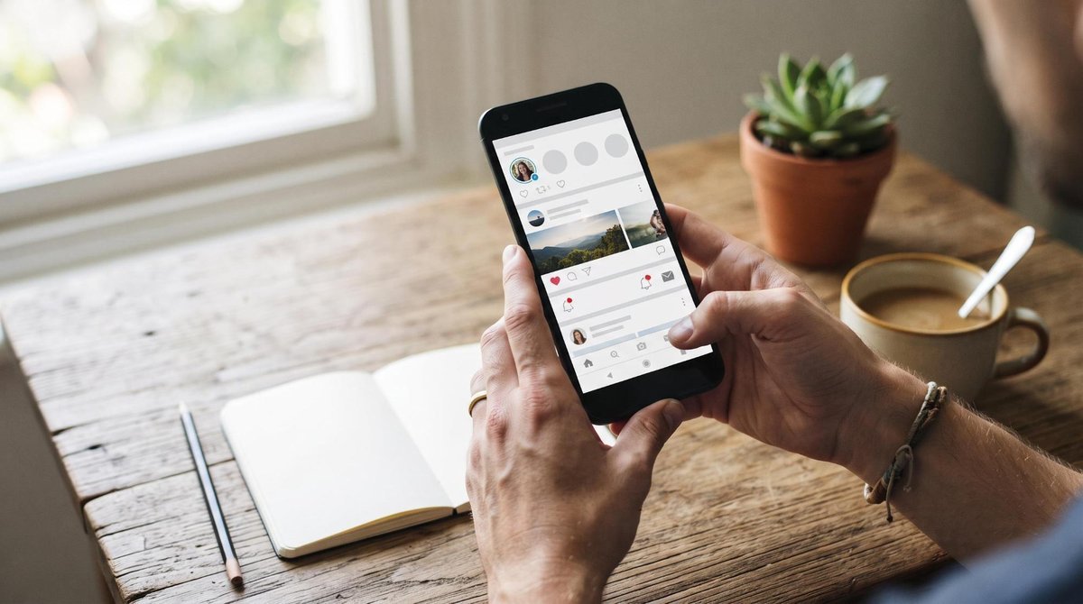Manos de una persona sosteniendo un smartphone con la pantalla mostrando notificaciones de redes sociales, sobre una mesa de madera rústica con cuaderno